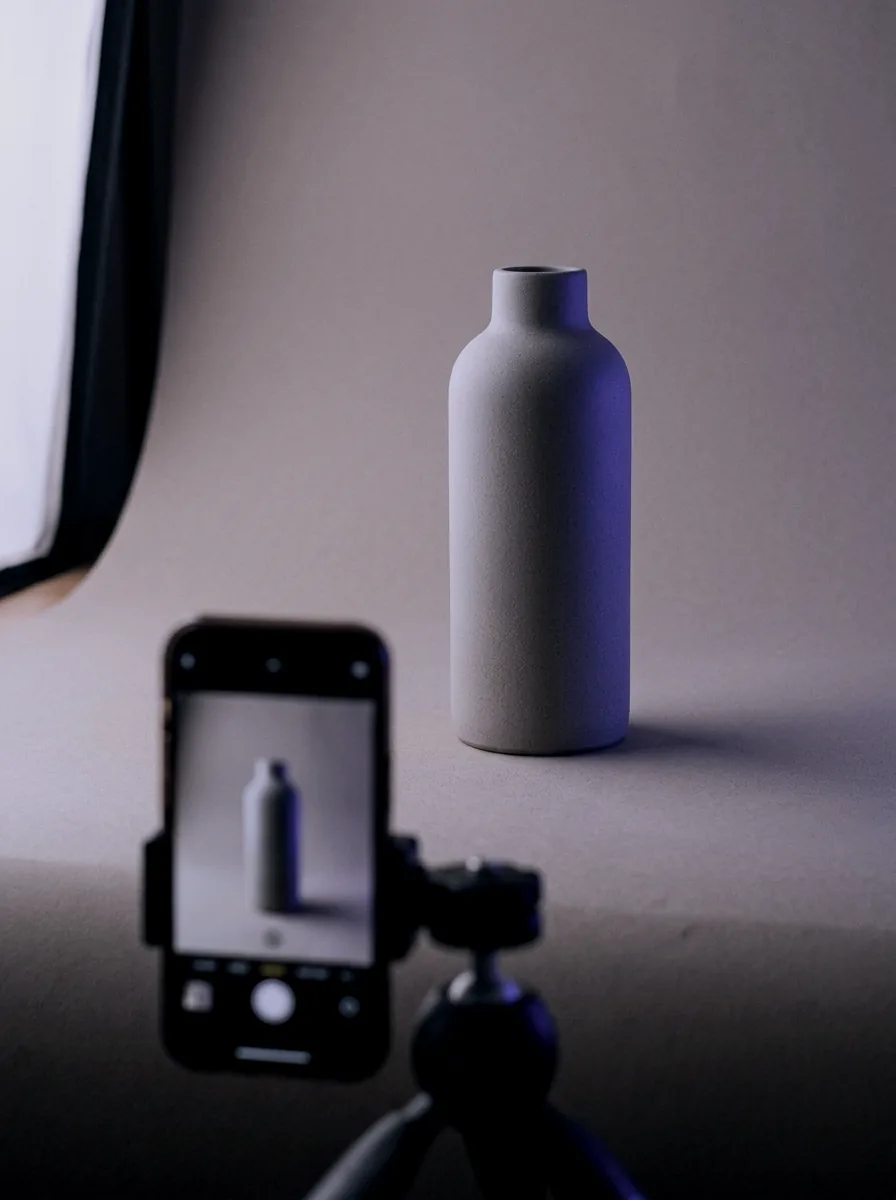 Phone on a small tripod filming a ceramic bottle for a product video
